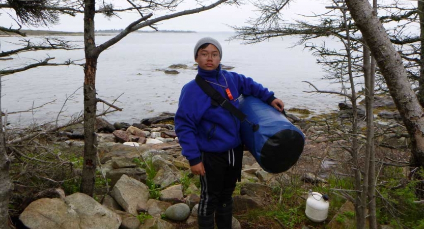 A person holds a duffle bag beside the shore of a lake